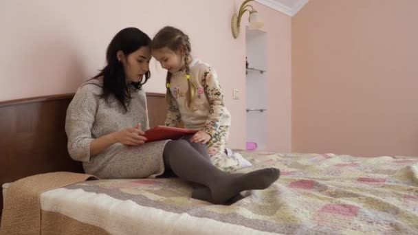 Jovem Mãe Senta Cama Trabalha Com Tablet Digital Menina Adorável — Vídeo de Stock