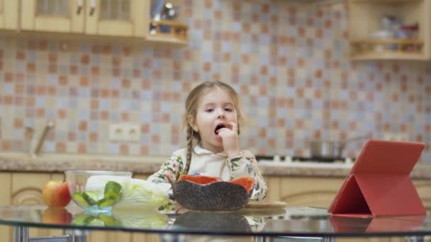 小さな女の子は台所でテーブルの前に立って野菜の一片を食べる サラダを作るためのかなりの子供の研究 コーデックを証明する — ストック動画