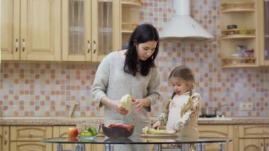 Genç anne küçük kızına mutfakta yemek yapmayı öğretiyor. Aile taze sebzelerle salata hazırlıyor ve onları kesme tahtasında kesiyor. Genç bir kadın boş zamanlarını küçük kızıyla evde geçirir. Kodlayıcıyı Düzenle.