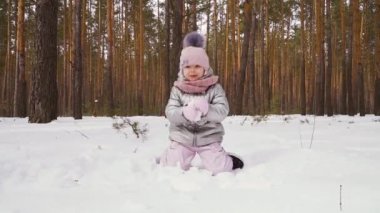 Tatlı küçük kız kış ormanında yürüyor. Pplayful karda tek başına eğleniyor. Çekici kız kar kusmaya çalışıyor. Yavaş çekimde. Kodlayıcıyı Düzenle.