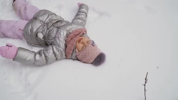 可爱的小女孩在冬天的森林里散步 爱玩的孩子一个人在雪地里玩得很开心 迷人的女孩躺在雪地上放松 慢动作 Prores Codec — 图库视频影像