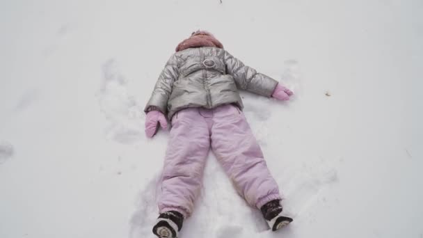 かわいい女の子は冬の森の中を歩く 子供は雪の上で一人で楽しむことができます 魅力的な女の子は雪の上に横たわっているとリラックス スローモーションだコーデックを証明する — ストック動画