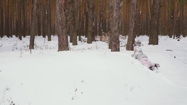 可爱的小女孩在冬天的森林里散步 顽皮的孩子一个人在雪地上玩得很开心 迷人的女孩在雪地上爬行 慢动作 Prores Codec — 图库视频影像