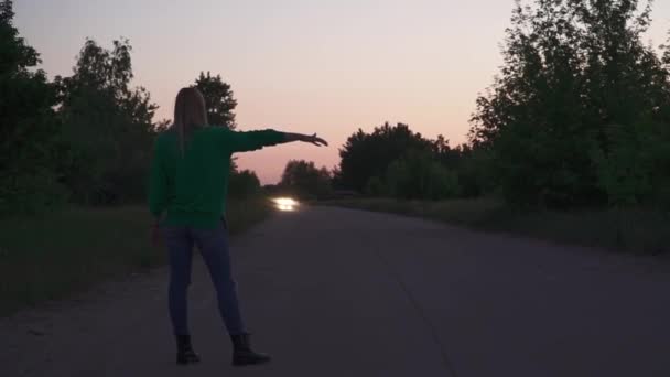緑のプルオーバーのブロンドの女の子が道に立っている 女性は髪を矯正し ゆっくりと踊り始めます 外で過ごす時間 — ストック動画