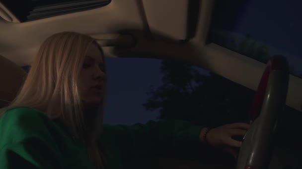緑のプルオーバーのブロンドの女の子が車を運転する 窓の外は夜遅く — ストック動画
