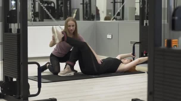 Αθλητικά κοκκινομάλλα γυναίκα ασχολείται με το γυμναστήριο με ένα ατομικό γυμναστή. Αθλητισμός, αποκατάσταση, υγεία. — Αρχείο Βίντεο