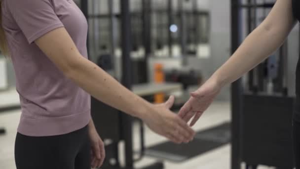 Entrenadora no reconocida y cliente estrechando las manos frente a un equipo de fitness en el gimnasio. Concepto de deporte, estilo de vida activo, salud . — Vídeos de Stock