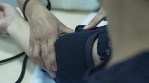 Unrecognized caucasian doctor measuring the pressure of an elderly woman sitting at the table in the office. Mature lady checking her health in the hospital. Concept of healthcare, treatment, medicine — Stock Video