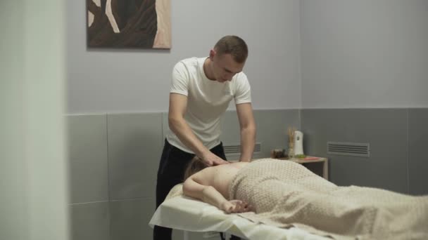 Professionele concentratedman masserende nek van de jonge vrouw die op een massagetafel legt. Meisje bij de massage therapeut. Concept van gezondheidszorg, behandeling, recreatie, geneeskunde. Problemen met de — Stockvideo