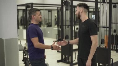 Genç profesyonel fitness eğitmeni ve orta yaşlı sporcu spor salonunda fitness ekipmanları önünde duran el sıkışma. Spor kavramı, aktif yaşam tarzı, sağlık