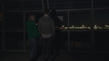 Genç adam ve kız gece uçağın kalkışını izliyorlar. Genç çift el ele tutuşup uçağın pistte ilerlemesini izliyor..