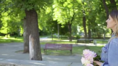 Genç güzel bir kadın yaz parkında yürüyor. Güzel sarışın doğanın tadını çıkarıyor. Kot ceketli çekici bir kız elinde şakayık kutusuyla dışarıda dinleniyor..
