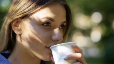 Tek kullanımlık fincandan kahve içen genç bir kadın. Güzel sarışınlar lezzetli içecekler içmeyi sever. Yakın plan. Yavaş çekim.