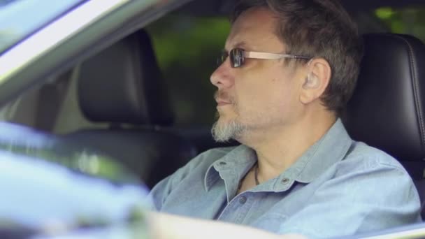 Człowiek Aparatem Słuchowym Kierownicą Samochodu Dorosły Mężczyzna Okularach Przeciwsłonecznych Rozgląda — Wideo stockowe