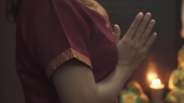 Güzel Taylandlı masöz kollarını bir masaj salonunda kavuşturdu. Kamera soldan sağa hareket eder. Mumlar yanar ve arkada bir Buda heykeli durur. Yakın plan..