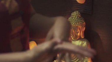 Masaj salonundaki kız elleriyle oynuyor. Mumlar yanar ve arkada bir Buda heykeli durur. Yakın plan..