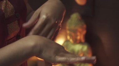 Masaj salonundaki öcüler onun elleriyle oynarlar. Mumlar yanar ve arkada bir Buda heykeli durur. Yakın plan..