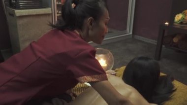 Masöz güzel bir kızın omuzlarına masaj yapar. Köşede masaj yatağının yanında mumlar yanıyor..