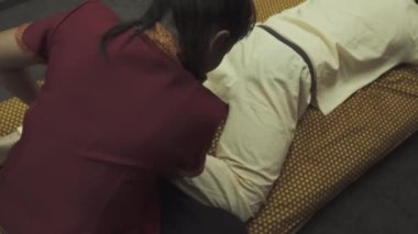 Masör masaj salonundaki bir adamın bacaklarına masaj yapıyor. Adam masaj yatağında yatıyor ve ayak masajı yaptırıyor..