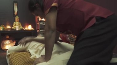 Tayland kaplıcasında bir adam için sırt masajı. Taylandlı masöz sırt masajı yapar. Masanın üzerinde yanan mumlar ve bir Buda heykeli var..