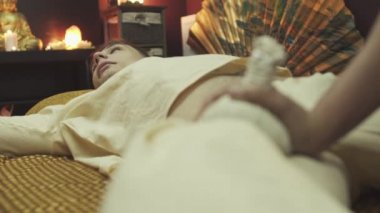 Adam masaj yatağında yatıyor. Yakışıklı çocuk bitkisel torbalarla ayak masajı yaptırıyor. Yakın plan..