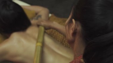 Bambu sırtıma masaj yapıyor. Tahta spa yatağında uzanan genç bir kadının vücudunda bambu masaj çubukları vardır. Yakın plan..