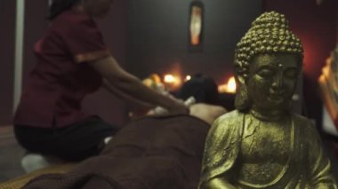 Bitkisel kese kullanan Tayland yemeği. Bitki torbaları, stres önleyici terapi. Masör bitkisel keseleri kadının vücuduna doğru itiyor. Ön planda bir Buda heykeli var. Yakın plan..