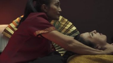 Taylandlı masöz güzel bir kıza kafa masajı yapıyor. Kadın Tayland masaj salonundaki masaj masasında yatıyor. Yakın plan..