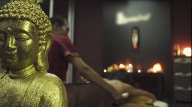 Bitkisel kesesi olan genç bayana Tayland masajı. Buda ön planda. Yakın plan..