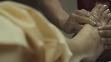 Taylandlı masöz genç bir kıza ayak masajı yapıyor. Kız masaj için yatakta yatıyor. Yakın plan..