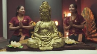 İki güzel Tayland masözü bir Buda heykelinin yanında nilüfer çiçekli bir poz veriyorlar. Kapat..