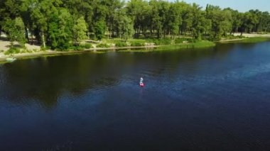 Genç adam nehir boyunca bir kanonun üzerinde ayakta yüzer. Kamerayı sağdan sola hareket ettir. Yukarıdan görüntüle.