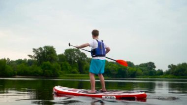 Genç adam nehir boyunca bir kanonun üzerinde ayakta yüzer. Adam küreklerini başının üstüne kaldırdı..