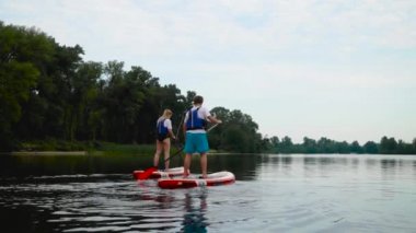 Güzel genç çift kıyıdaki kanoların üzerinde yüzüyor. Gençler aktif olarak suyun üzerinde dinleniyorlar..