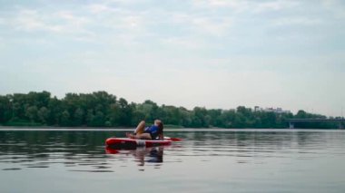 Güzel genç kız kanoya uzanıp nehirde yüzüyor. Arka planda otomobil köprüsü.