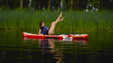 Güzel genç kız suda bir kanoya uzanıyor. Kız bacak ve mide egzersizi yapıyor..
