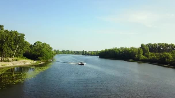 川沿いのカメラの動き 堤防沿いの川や木々の美しい景色 カメラはモーターボートに向かって移動します 上からの眺め — ストック動画