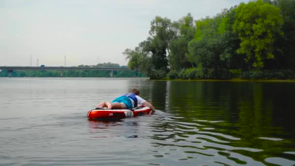 英俊的年轻人躺在皮划艇上 用手划船 背景上的汽车桥 — 图库视频影像
