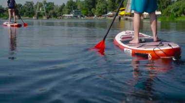 Erkek ve kız kardeş nehir boyunca kano yapıyorlar. Önünde şehir plajı var..