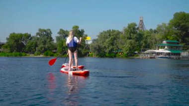 Erkek ve kız kardeş nehir boyunca kano yapıyorlar. Önünde şehir plajı var..