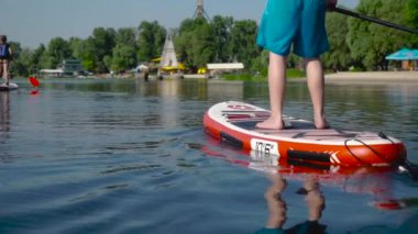 Erkek ve kız kardeş nehir boyunca kano yapıyorlar. Önünde şehir plajı var..