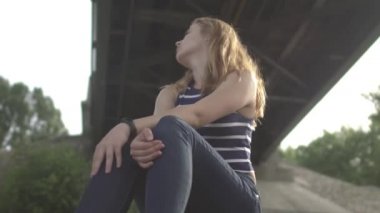 Köprünün altında oturan üzgün kız. Köprünün altında güzel bir kadın oturuyor. Kadın dışarıda vakit geçiriyor. Dişi, güzel manzaraya hayran..