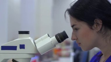 Laboratuar teknisyeni mikroskoba bakıyor. Kapat..