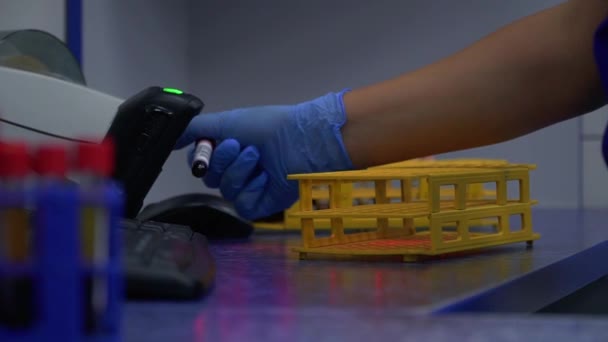 青いゴム手袋スキャンバーコードの女性の手と試験管を閉じるためにラックにチューブを置きます 研究室で研究を行う 医療スローモーション カメラの動きが正しい — ストック動画