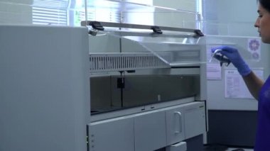 Mavi üniformalı ve lastik eldivenli genç kadın laboratuarda çalışan makinenin kapısını açıyor ve içine yakından bakıyor. Laboratuvarda araştırma yapıyorum. Bilim, meslek, sağlık. Yavaş çekim