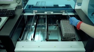 Kadının eli test tüpleriyle rafları makineye yerleştiriyor. Laboratuvardaki elektronik ekipman. Araştırma makineleri, yeni teknoloji. Bilim, meslek, sağlık konsepti
