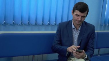 Modern bir özel klinikte koridorda oturan yetişkin adam cep telefonunu kullanarak analizinin sonuçlarını bekliyor. Adam sağlığını kontrol ediyor. Sağlık hizmetleri kavramı