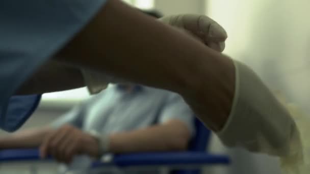 看護師の手を手袋に入れ 大人のハンサムな患者の背景にある肘掛け椅子に座っての血を取る準備を出血 血液検査科学 — ストック動画