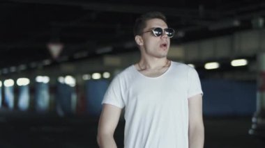 Beyaz tişörtlü, güneş gözlüğü takan ve yeraltı otoparkında duran mutlu adamın portresi. Kendine güvenen bir adam dışarıda yalnızdır.