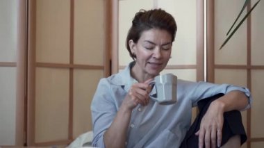 Zarif iyi giyimli olgun bayan portre çay veya kahve içme ve arkadaşı ile konuşurken. Evde dinlenen kadın. Sağlıklı yaşam, dinlenme, mutlu bir hayat. Olgun kız arkadaşlar boş zaman. Yavaş çekim.